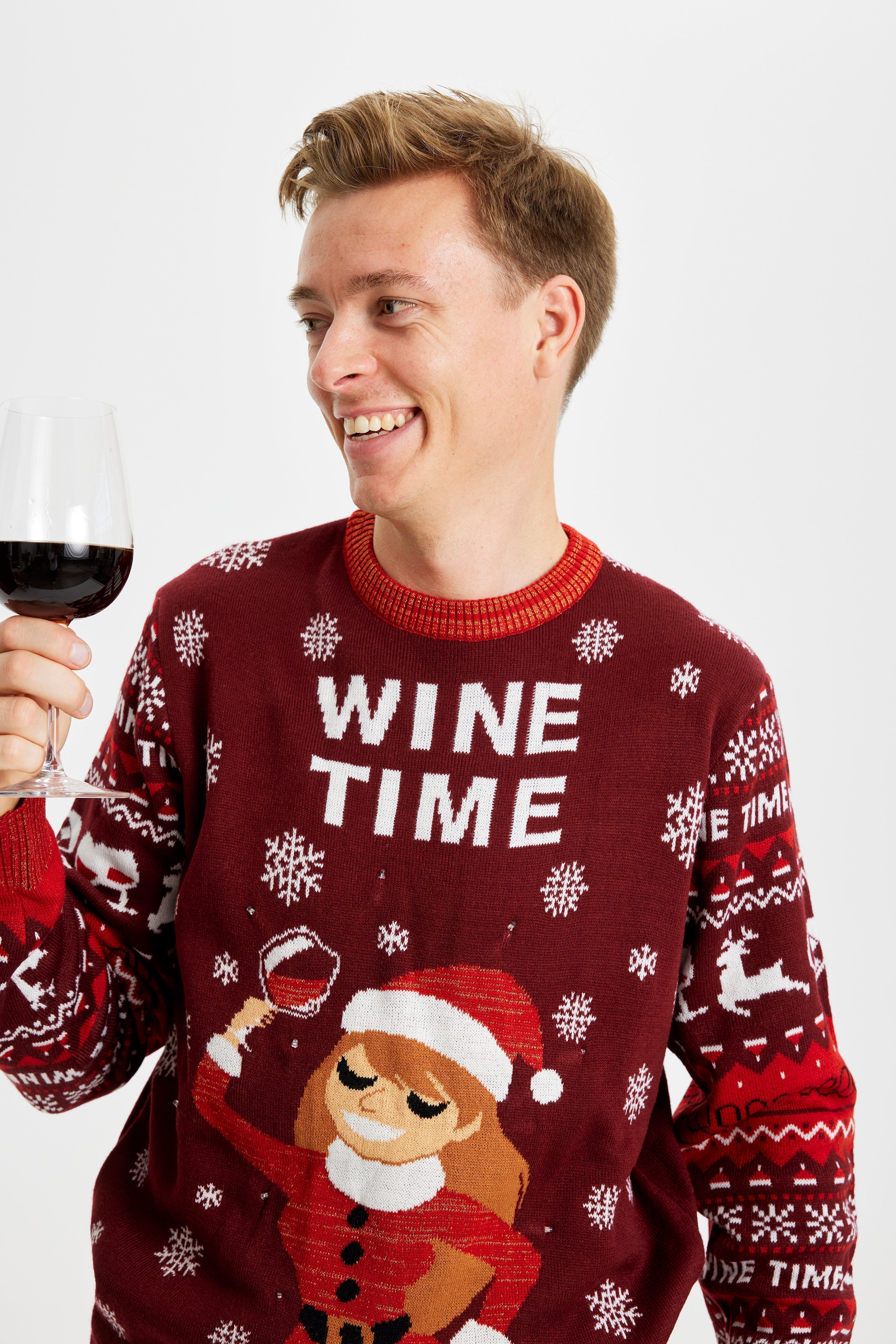 Un homme souriant avec un verre de vin portant un pull rouge de Noël avec la citation